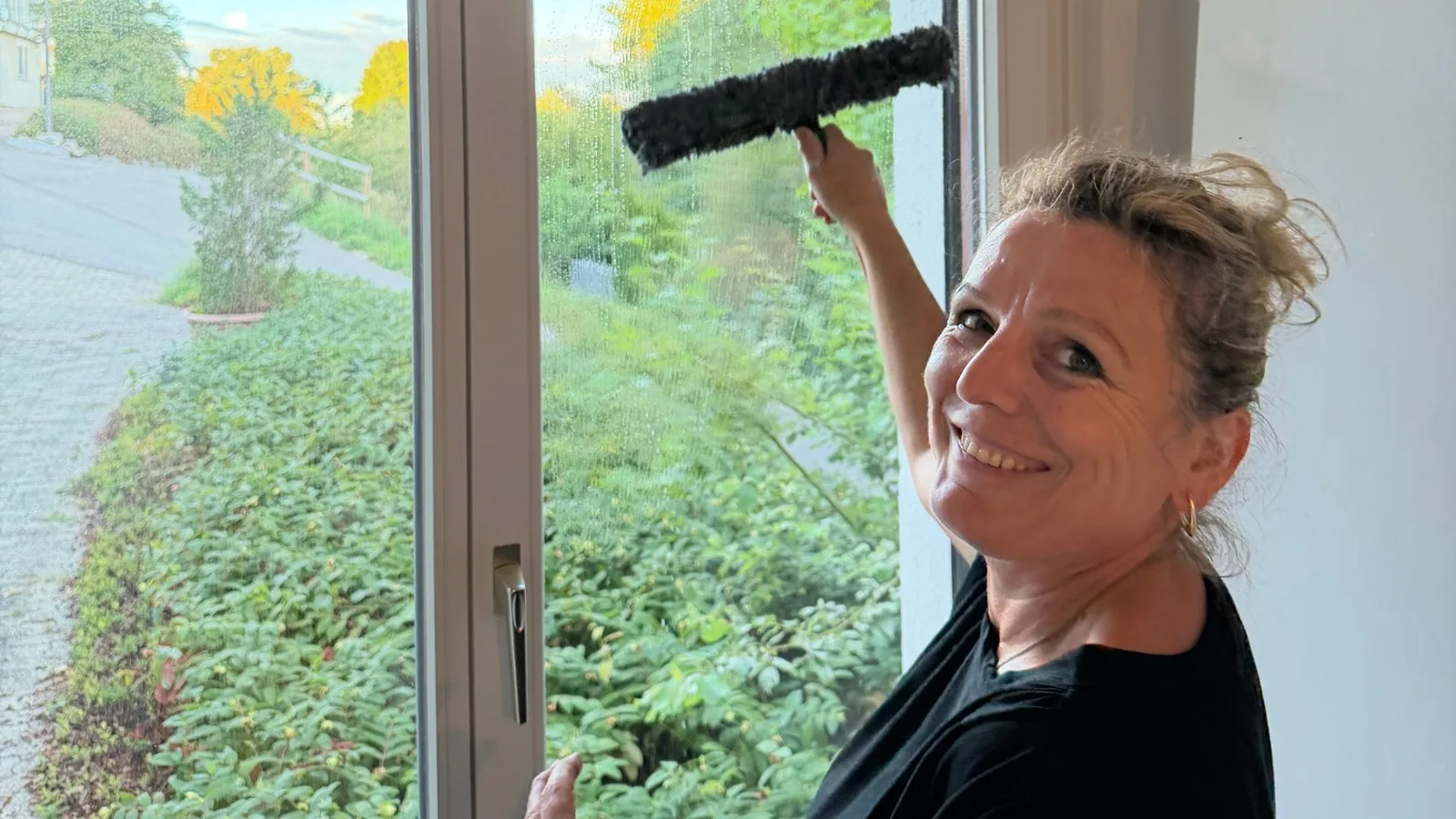 Gjemile Shala reinigt ein Fenster mit dem Abzieher