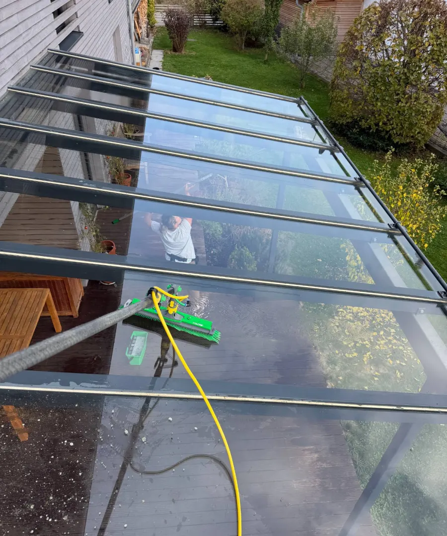 Glasdach einer Terrassenüberdachung wird mit Reinwasser und Teleskopbürste gereinigt